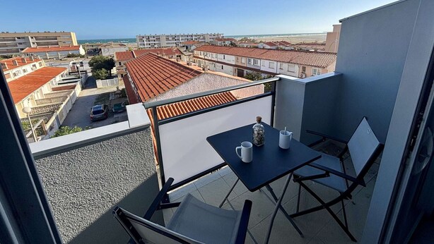 Een balkon met een tafel en stoelen, met uitzicht op een woonwijk met rode dakpannen.