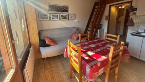 Una habitación acogedora con una mesa de madera, sillas, un sofá y una escalera que lleva a una cocina.