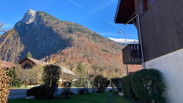 Una montaña con cielo despejado, un edificio de madera con balcón y un jardín cuidado.