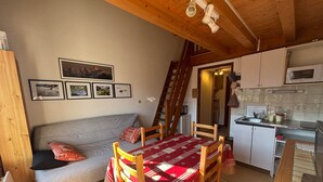 Una habitación acogedora con sofá, una mesa de comedor con sillas, una zona de cocina con microondas y una escalera que sube a un nivel superior.