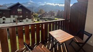 Un balcón con una mesa y sillas de madera, con vistas a una zona residencial con casas y montañas al fondo.