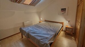 Un dormitorio con techo inclinado, una cama, una mesita de noche, una lámpara y un cuadro enmarcado en la pared.