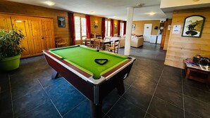 Ein Billardtisch in einem Raum mit Holzwänden, einem Essbereich und einer Küche im Hintergrund.