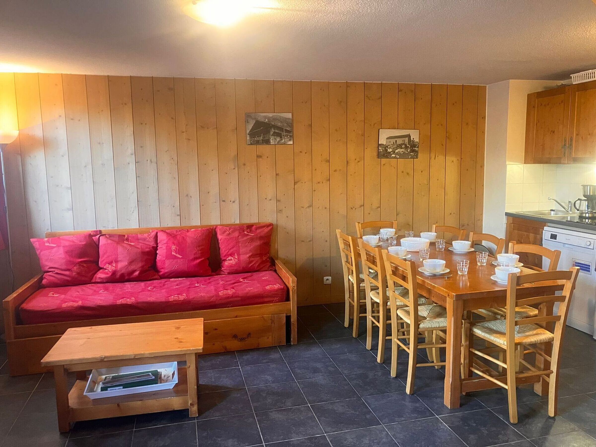 A cozy room with a wooden sofa, a dining table set with white dishes, and a kitchen area.
