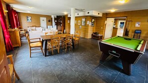 Ein Zimmer mit Billardtisch, Esstisch mit Stühlen, einer Couch und einer Küchenzeile.