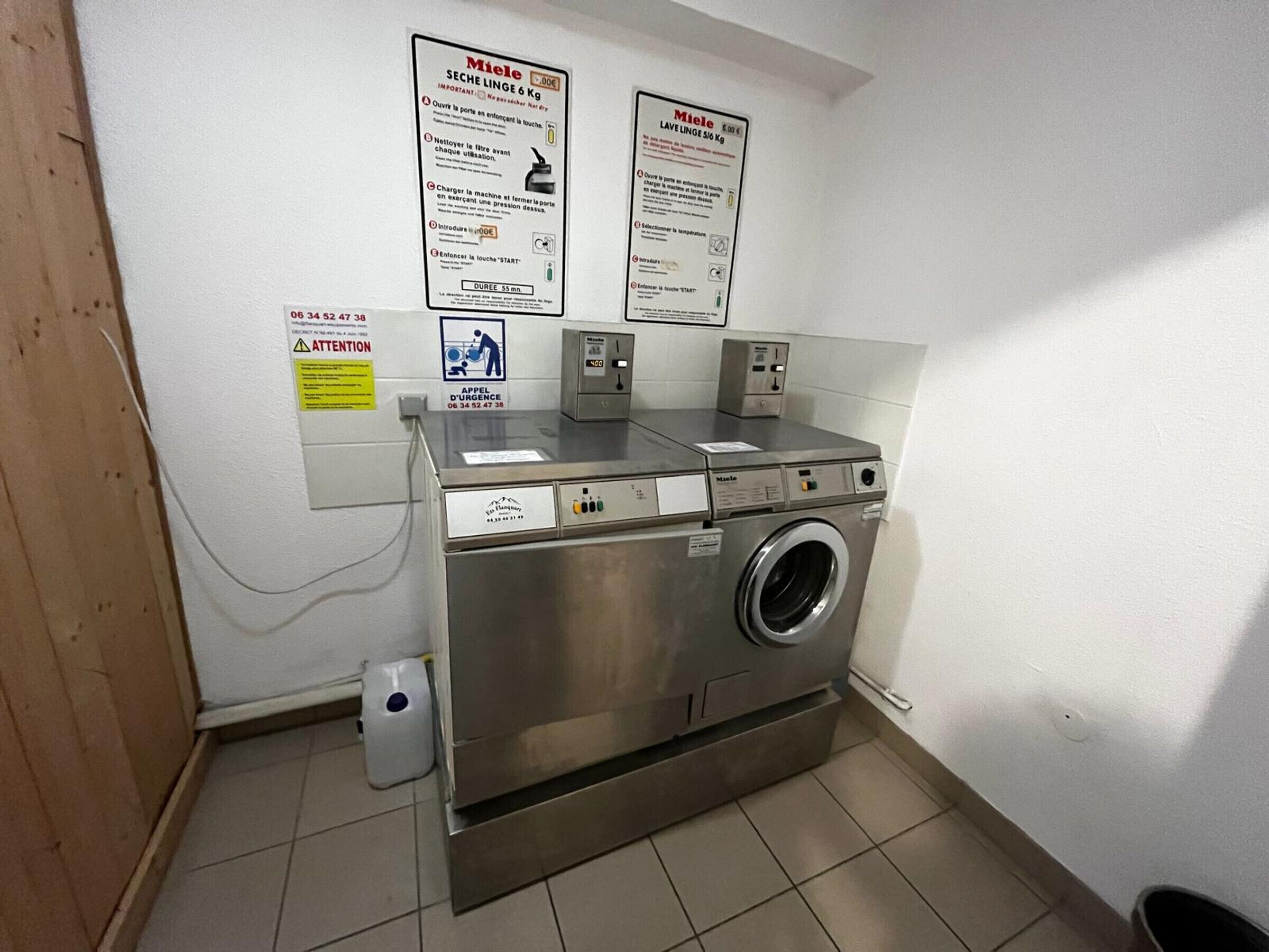 A laundry facility with a front-loading washing machine, a dryer, and two instructional posters on the wall.