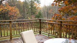 Eine Holzterrasse mit einem Stuhl und einem Tisch, umgeben von Herbstlaub.