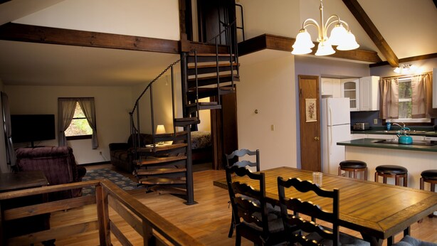 Ein geräumiger Wohnbereich mit einem Holzessttisch, einer Treppe und einer Küche inklusive Kühlschrank und Spüle.