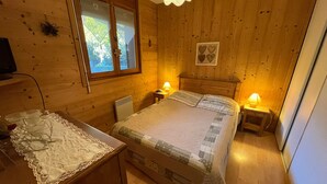 Una habitación acogedora de madera con una cama, lámparas de noche, un escritorio con mantel de encaje y una ventana con cortinas con forma de corazón.