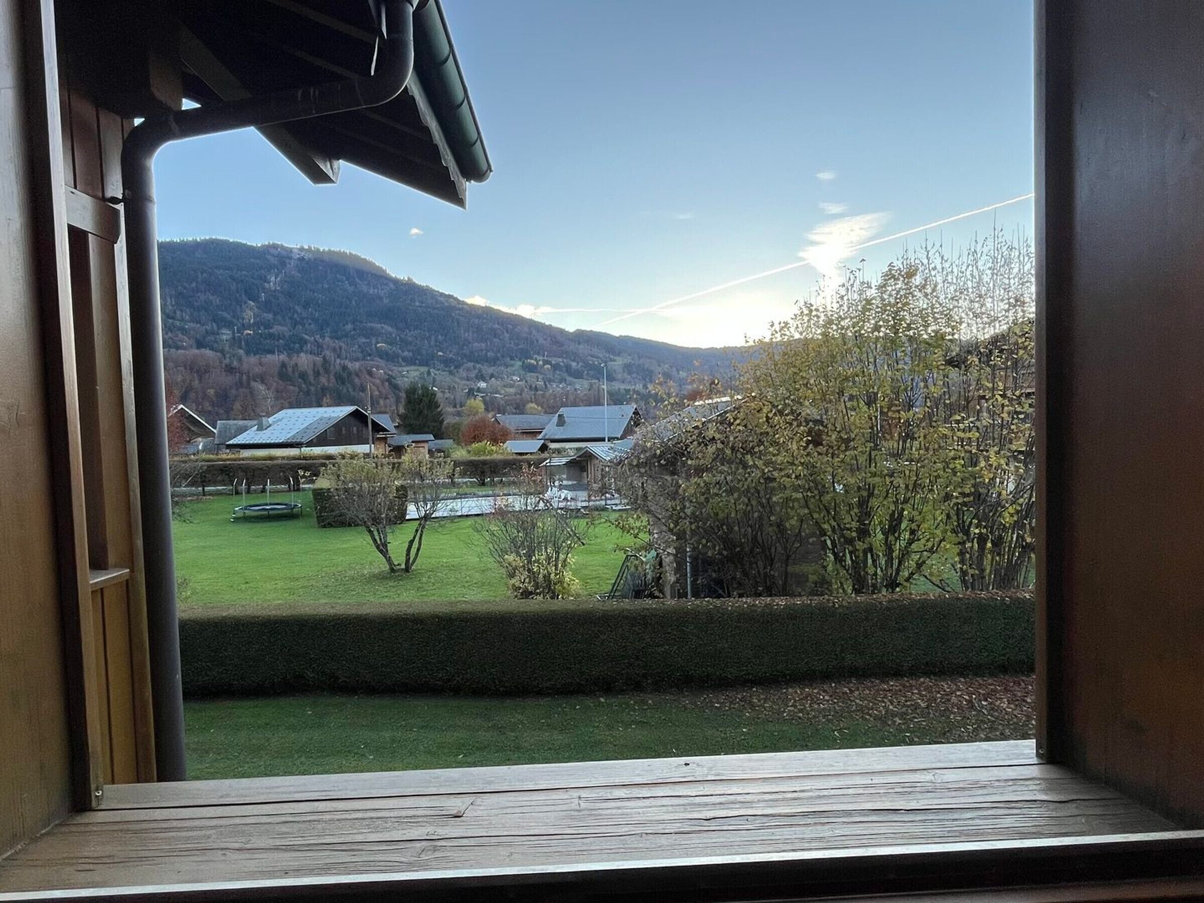 A view from inside a building looking out to a rural landscape with houses, a green field, and hills in the distance.