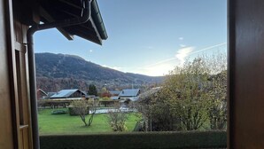 Vista desde el interior de un edificio hacia un paisaje rural con casas, un campo verde y colinas a lo lejos.