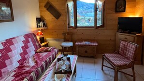 Interior acogedor de una cabaña con paredes de madera, un sofá, una mesa de comedor con una bandeja de tazas, una silla y un televisor.