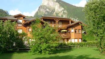 A wooden chalet with multiple balconies, surrounded by lush greenery and a mountain backdrop.