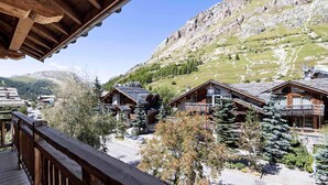 Et fjeldhotel med træarkitektur, en balkon og udsigt over de omkringliggende bakker og træer.