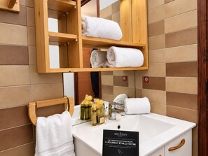 A bathroom with a wooden shelf holding towels, a sink with toiletries, and a sign. - Bright studio at slope's foot, 3 pers - Méribel (Méribel)