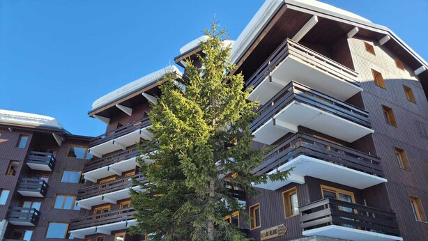 En hotelbygning med flere etager, altaner, en stenfassade og et skilt, der angiver indgangen til et skiområde.
