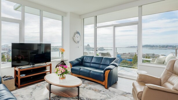 Ein großzügiges Wohnzimmer mit großem Fernseher, bequemen Sitzgelegenheiten und Blick auf ein Gewässer.