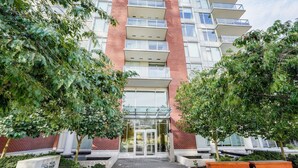 Ein modernes Mehrfamilienhaus mit zentralem Eingang, umgeben von Grünflächen und einem gepflasterten Weg.
