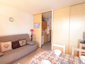 A cozy living room with a sofa, a dining table with chairs, a kitchen in the background, and a clock on the wall. - Studio for 4 pers with balcony at ski slopes (Flaine)