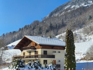 A multi-story chalet with a sloped roof, wooden balconies, and a view of a snowy mountain landscape. - Spacious 4-bedroom apartment in Abondance with WIFI and parking (Abondance)