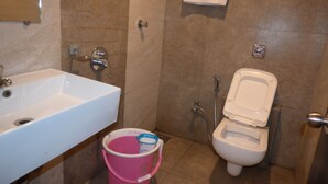 Un baño con lavamanos, inodoro y un cubo rosa.