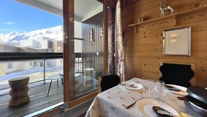 Un comedor con una mesa dispuesta para dos personas, interior de madera, vista a las montañas y puerta de cristal que da al exterior.