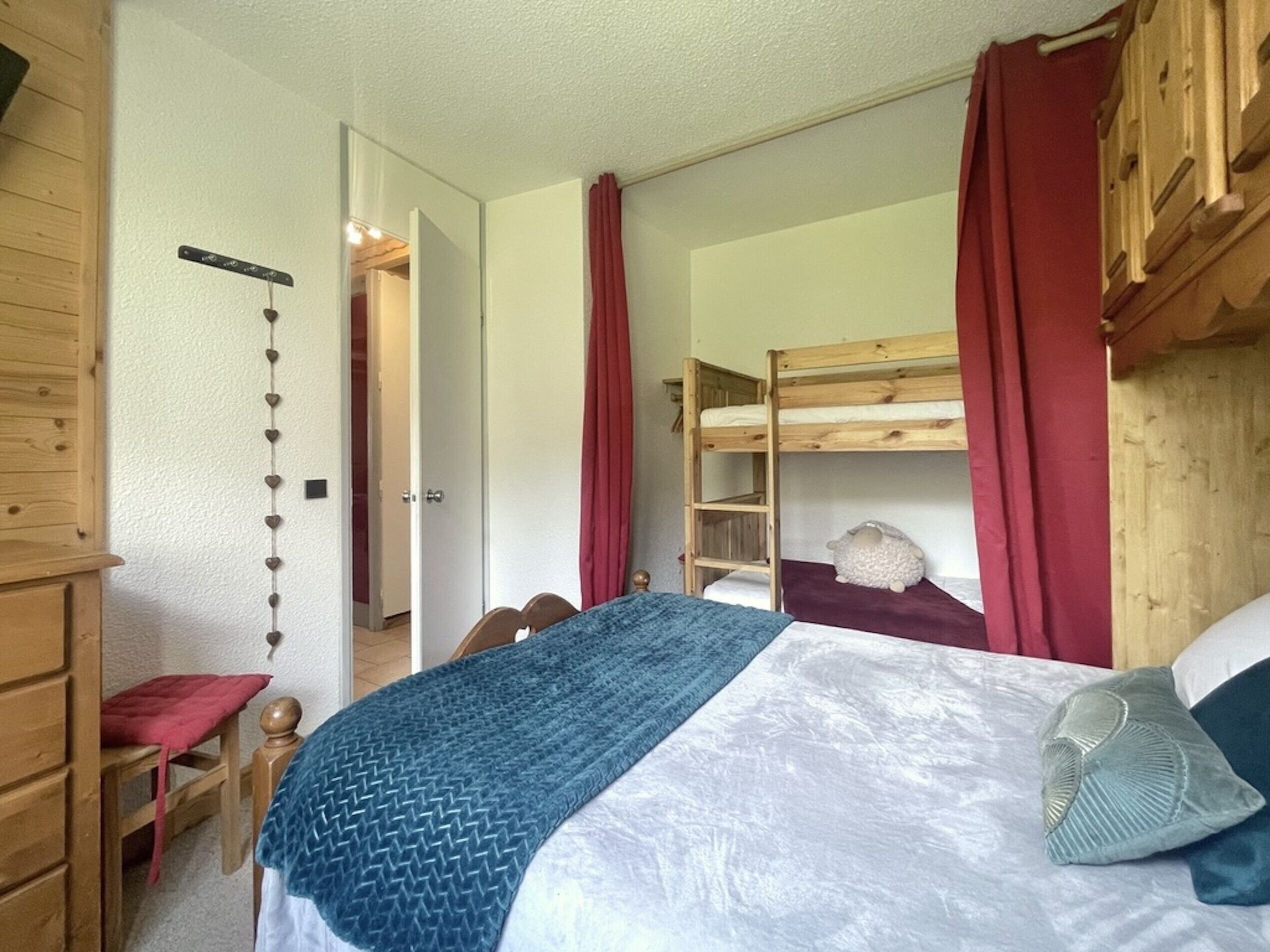 Una habitación con una cama doble, un armario de madera, una silla y una puerta que da a otra estancia.