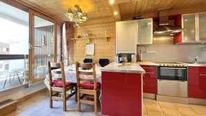 Una cabaña de madera acogedora con comedor que incluye una mesa y sillas, una cocina con electrodomésticos modernos y un amplio ventanal con vistas a una terraza.