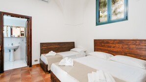 A bedroom with two beds, a wooden headboard, a window with a view, and a bathroom with a sink and mirror.