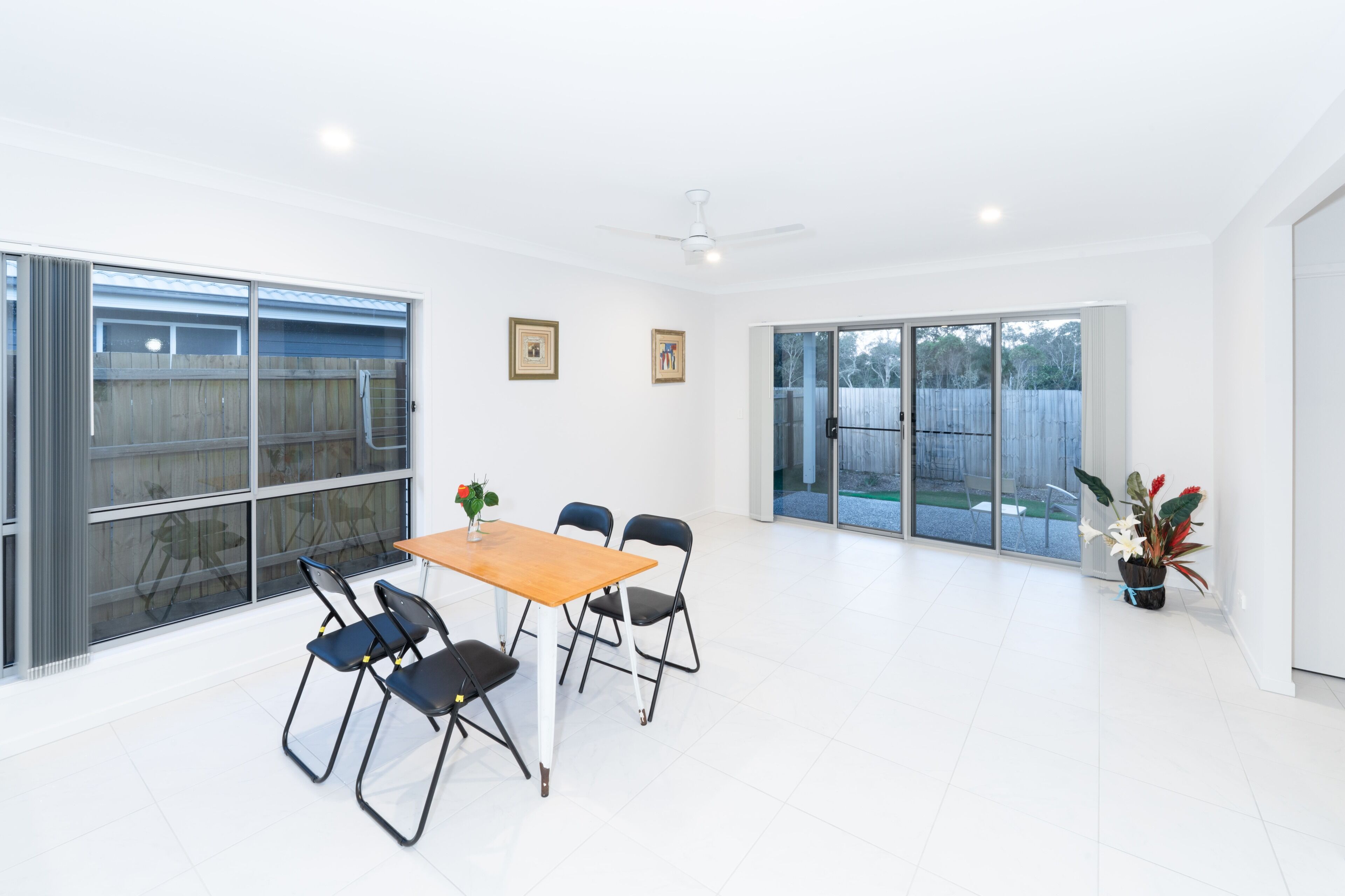 A spacious room with a large sliding glass door leading to an outdoor area, a small table with chairs, and a ceiling fan.