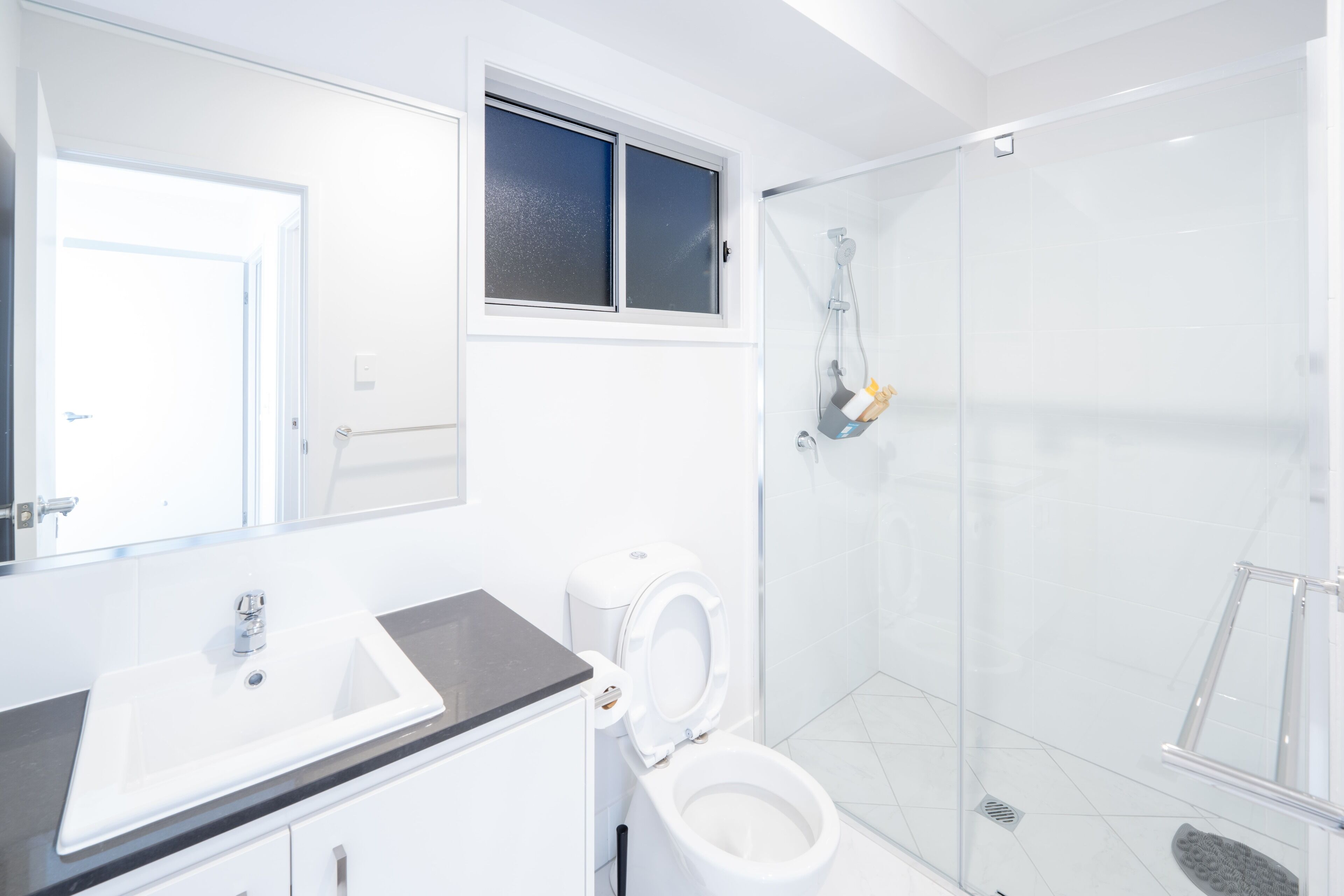A modern bathroom with a white sink, toilet, and glass shower enclosure.