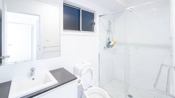 A modern bathroom with a white sink, toilet, and glass shower enclosure.