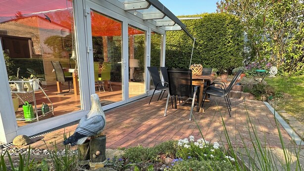 Eine Terrasse mit Glasveranda, einem Holztisch und Stühlen.