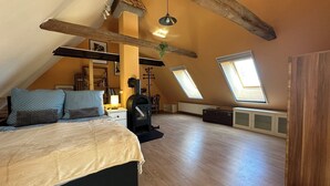 Ein geräumiges Schlafzimmer im Dachgeschoss mit einem großen Bett, Dachfenstern, einem Kaminofen und einer gemütlichen Leseecke.