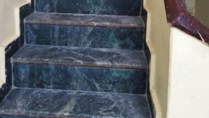 Una escalera con peldaños de mármol oscuro y barandilla de madera.