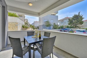 A balcony with a table and chairs, overlooking a street with parked cars and buildings. - One-bedroom Apartment with Balcony - C1 Infinity (Novalja)