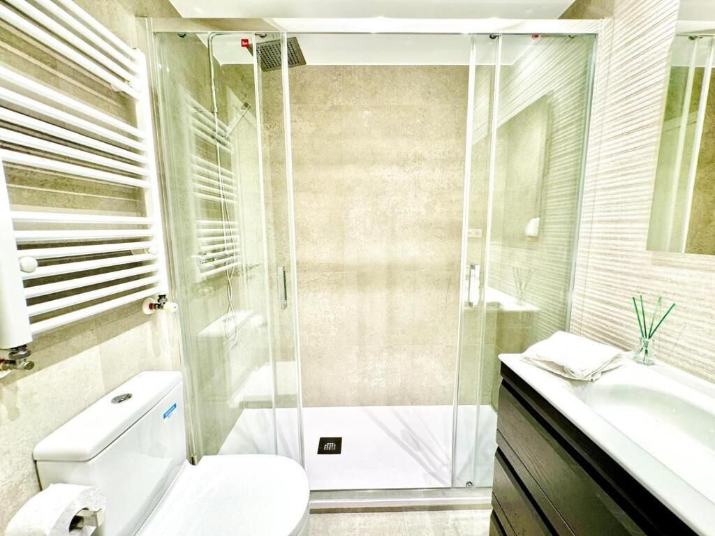 A modern bathroom with a glass-enclosed shower, a toilet, a sink with a towel, and a mirror.