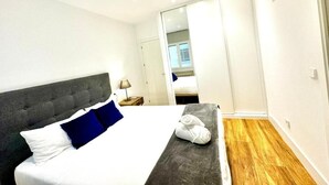 Une chambre moderne avec un grand lit, une tête de lit grise et un plancher en bois.