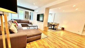 Un salon moderne avec un canapé d’angle, une table à manger et un téléviseur fixé au mur.