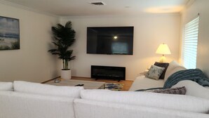 En stue med en hvid sofa, et fladskærms-tv, en pejs, en potteplante og en lampe.
