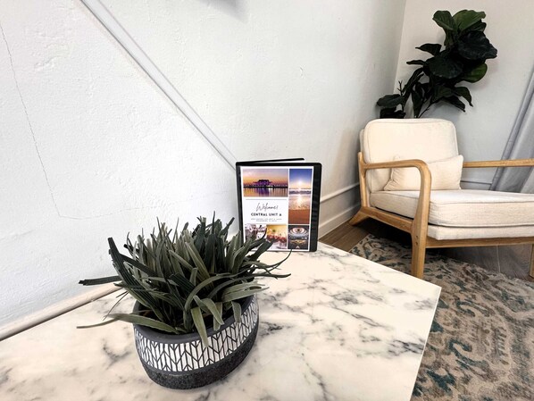 A potted plant on a marble table, a framed welcome sign, a wooden chair, and a large potted plant against a white wall. - Grand Central Kava Loft Walk to Vibes (St. Petersburg)