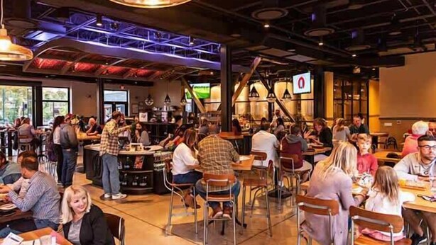 A busy restaurant with high ceilings, exposed beams, and a mix of seating arrangements including tables and chairs. - Grand Central Kava Loft Walk to Vibes (St. Petersburg)