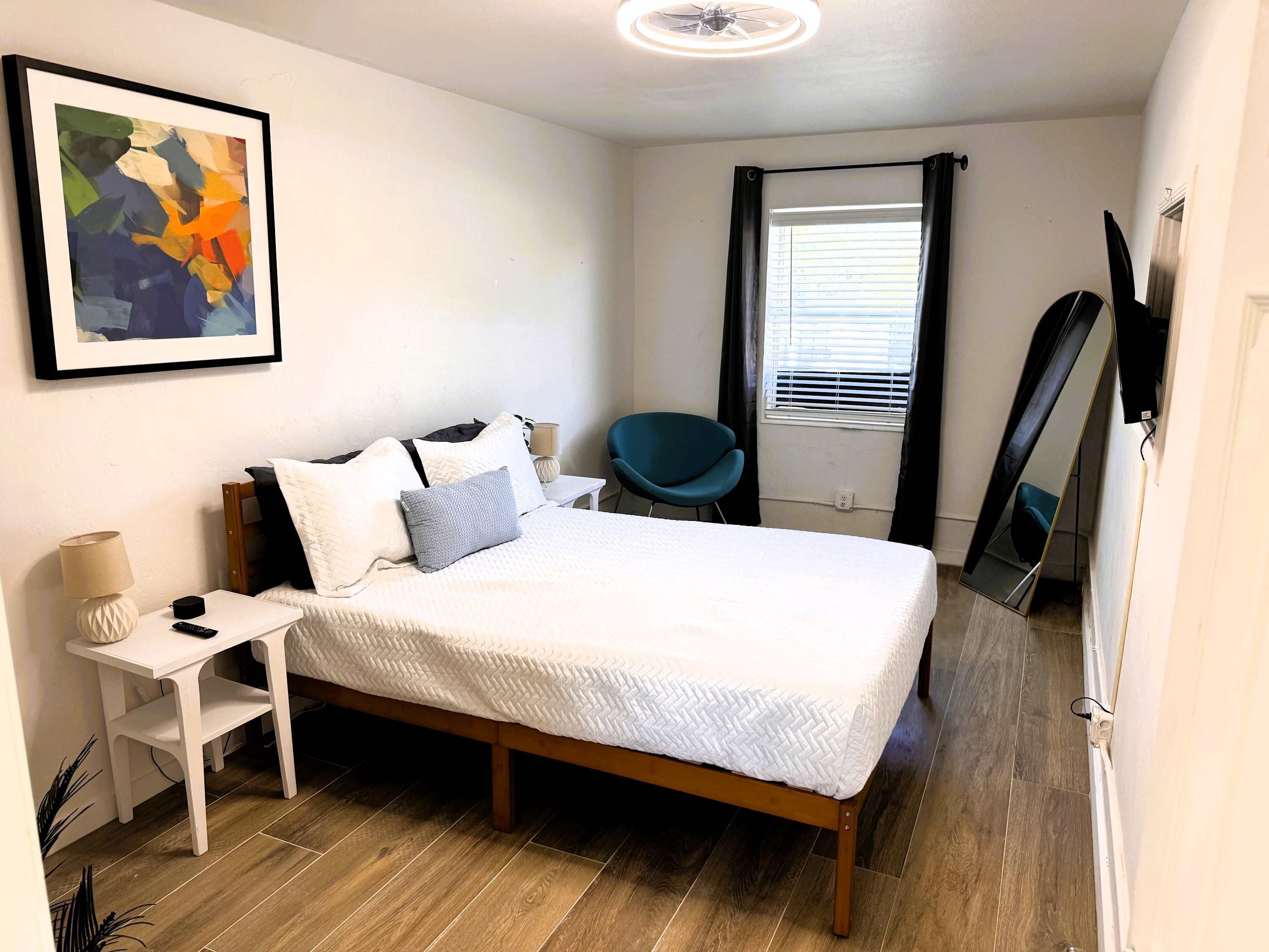 Ein ordentlich eingerichtetes Schlafzimmer mit Bett, Nachttisch, Stuhl und einem großen Spiegel.