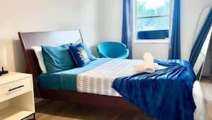 A neatly arranged bedroom with a bed, a bedside table, and a window with curtains. - Grand Central Kava Loft Walk to Vibes (St. Petersburg)