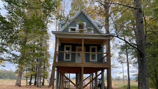 Ein hölzernes Turmhaus mit Balkon, umgeben von Bäumen und einem von Blättern bedeckten Boden.