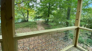Eine Holzterrasse mit Metallgeländer, die auf einen bewaldeten Bereich mit einem Weg und herabgefallenen Blättern blickt.