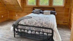 Ein Schlafzimmer einer Holzhütte mit einem Bett, zwei Fenstern und einer schrägen Decke.