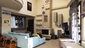 A spacious living room with a light blue sofa, wooden chairs, a fireplace, a television, and a balcony. - The Sunset Haven Kastoria Modern Lake Elegance (Kastoria)