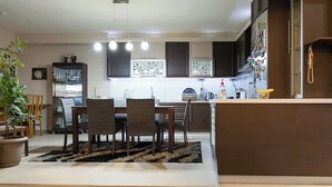A modern kitchen with dark cabinets, a central island, and a dining area with chairs and a rug. - The Sunset Haven Kastoria Modern Lake Elegance (Kastoria)
