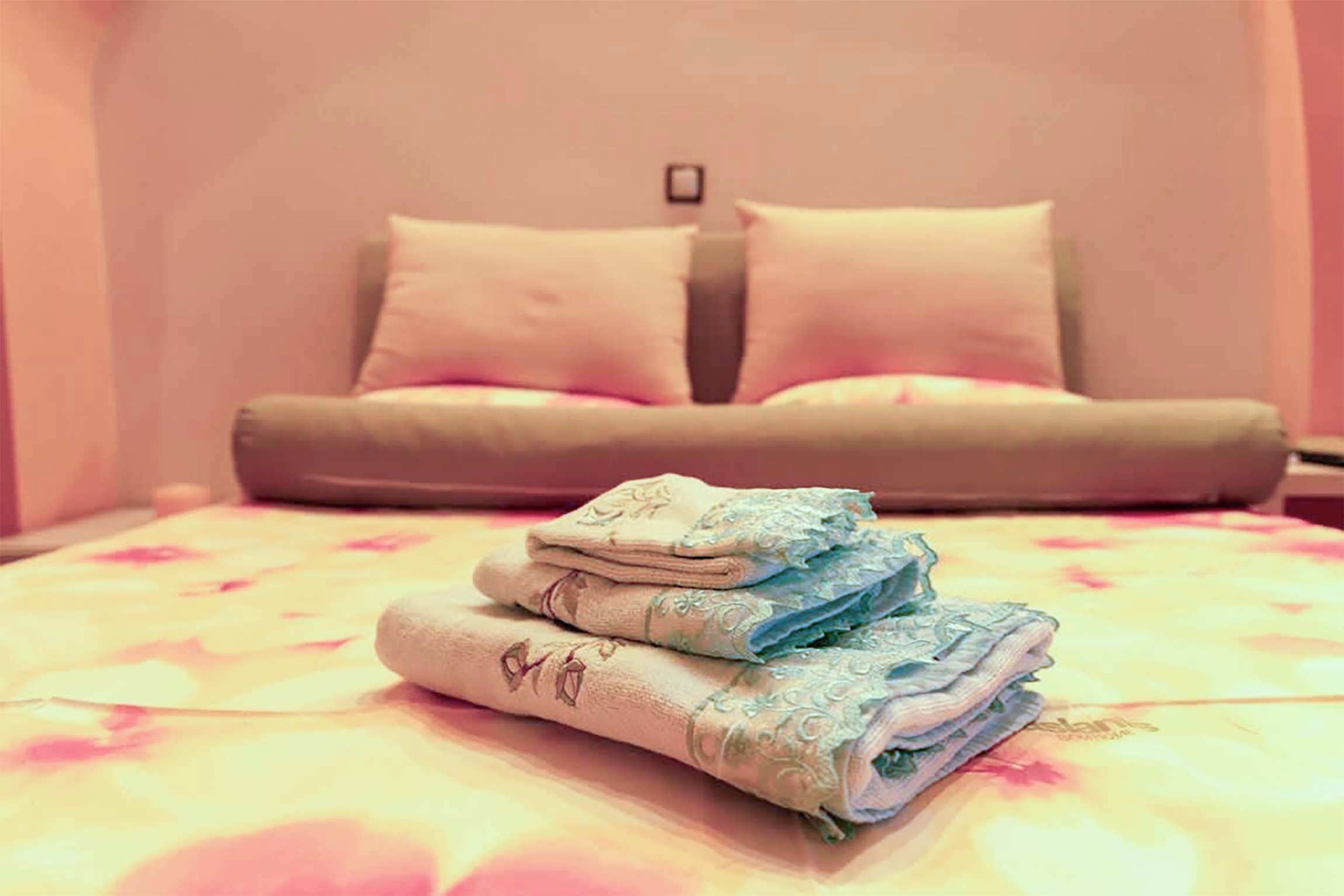 A neatly made bed with a floral-patterned bedspread and a stack of folded towels.